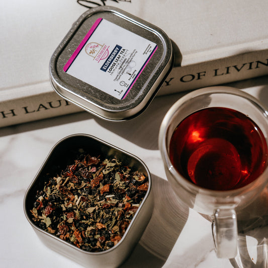 Tea tin with tea leaves, a cup of tea, and a book on a marble surface.