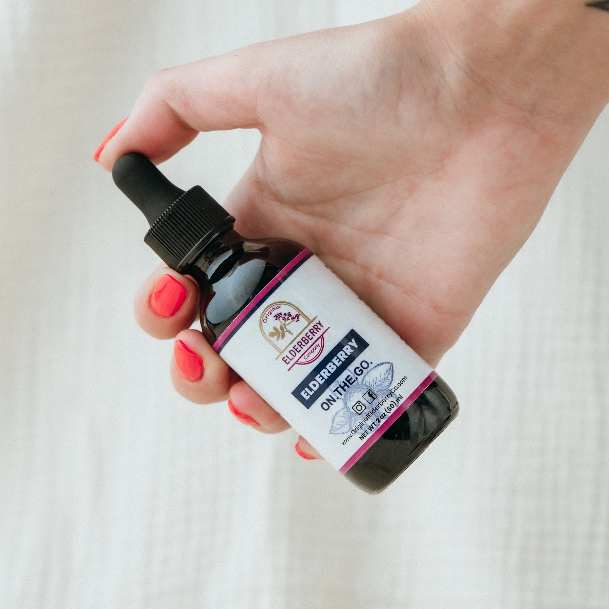 Hand holding a bottle with a dropper against a neutral background