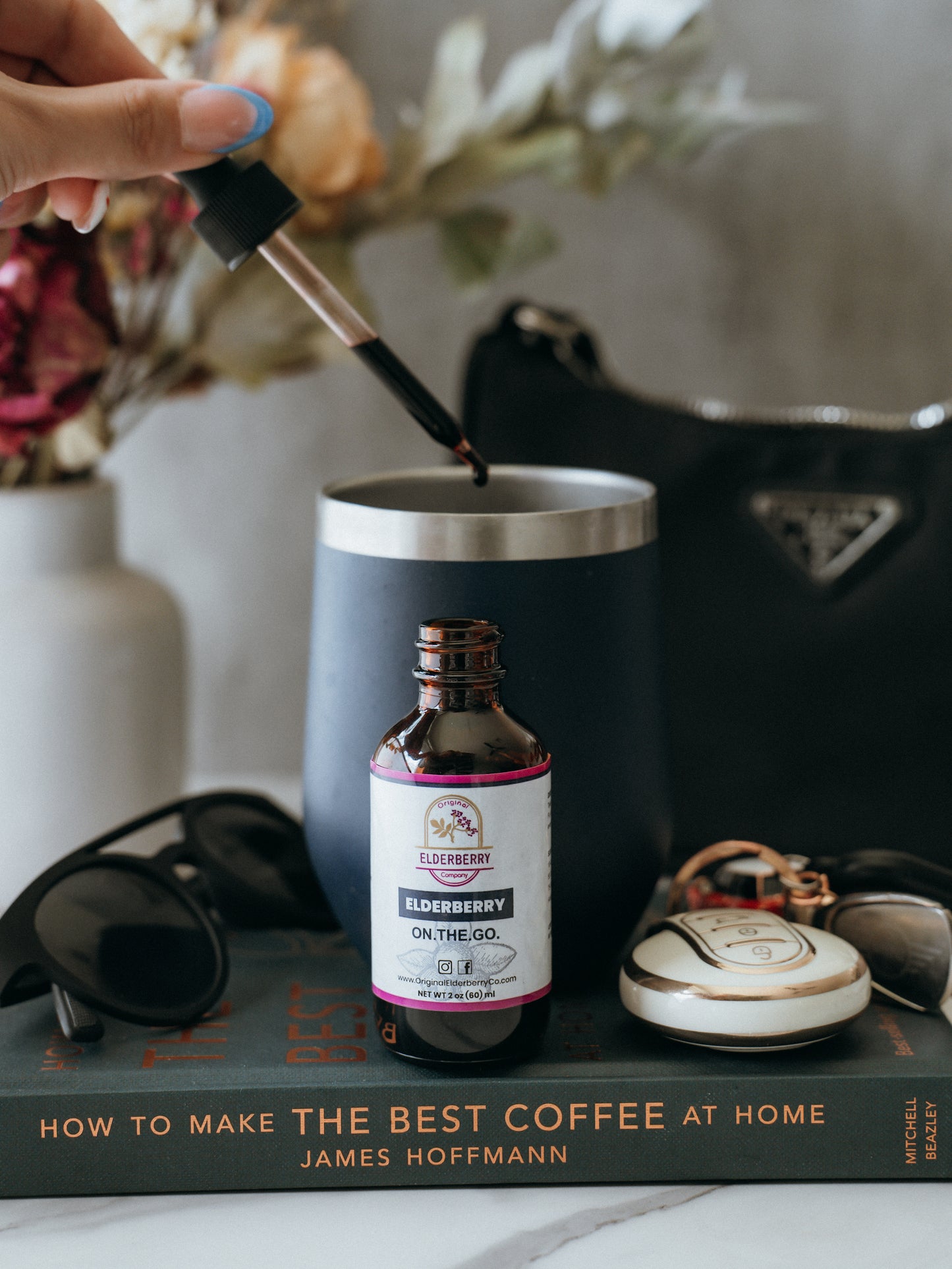 Person pouring liquid into a black mug with a bottle labeled 'On The Go' on a book titled 'How to Make the Best Coffee at Home'.