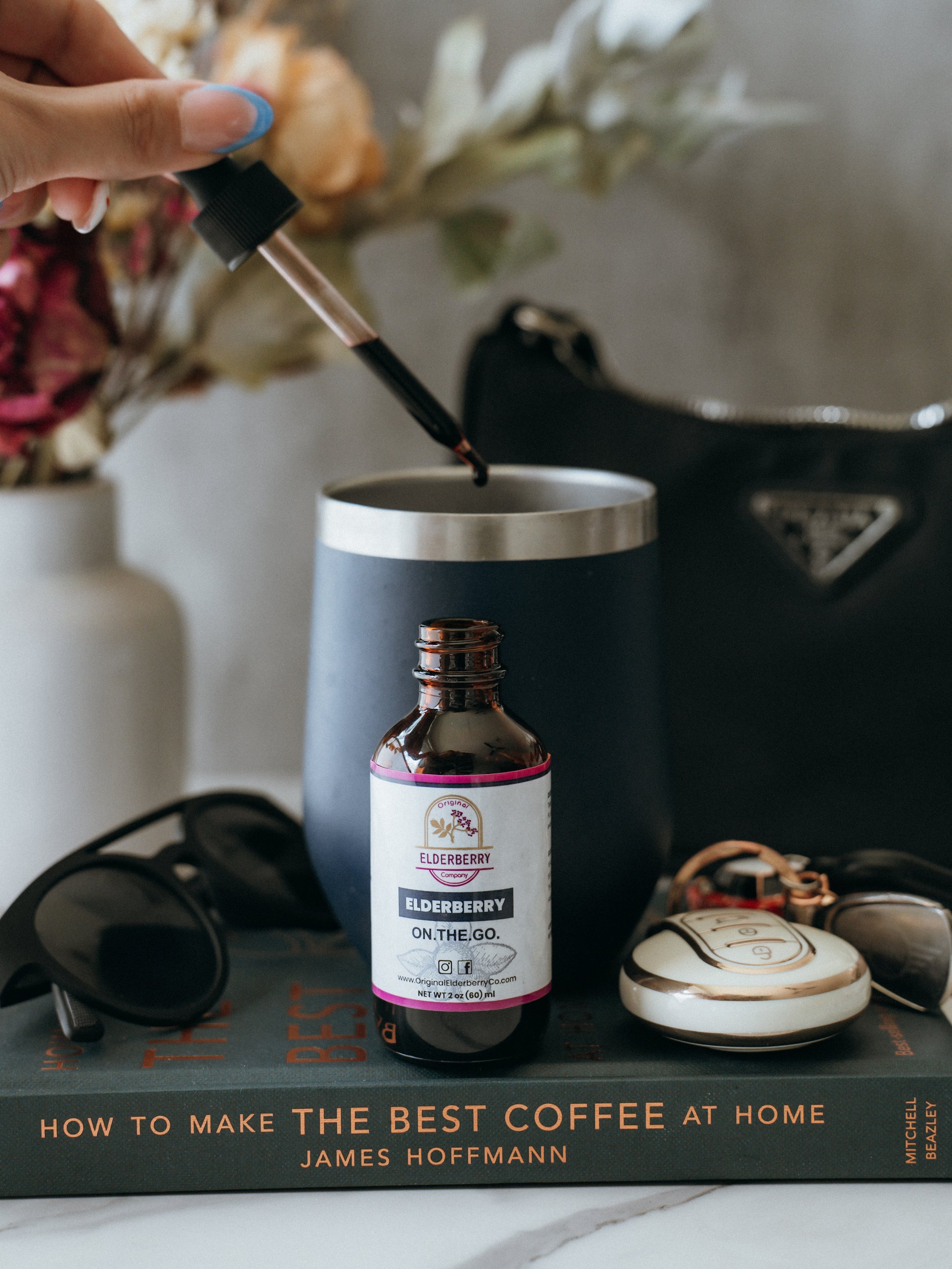 Person pouring liquid into a black mug with a bottle labeled 'On The Go' on a book titled 'How to Make the Best Coffee at Home'.